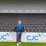 Paul Gow by Bromley Football Club Pitch side CJC signage at Bromley FC